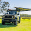 small rooftop tent attached to car parked next to tree in open grass area